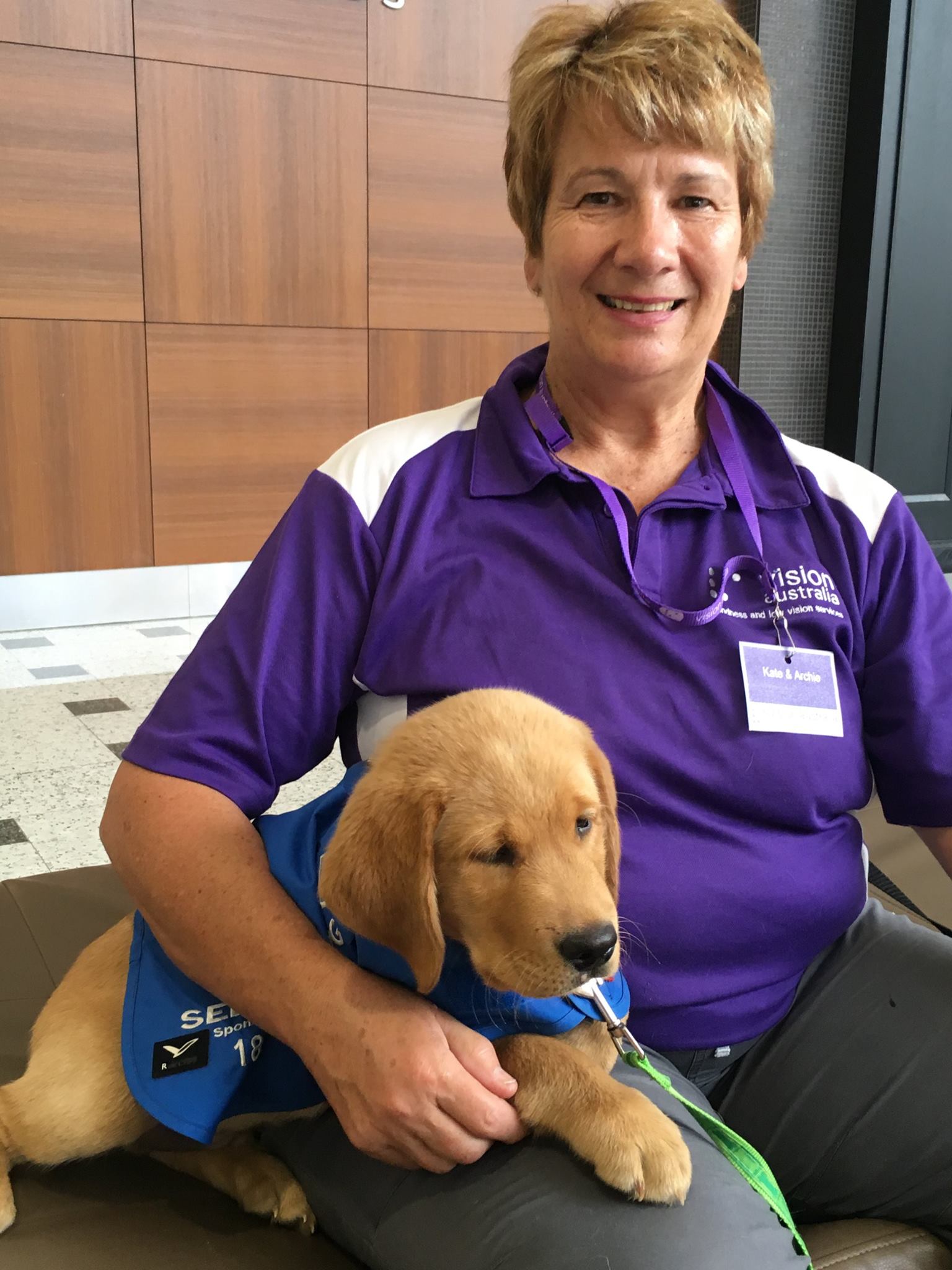 "Kate wearing old Vision Australia branding with a puppy she is fostering by her side"