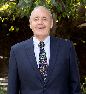 Vision Australia CEO Ron Hooton is smiling at the camera. He is dressed in a dark blue suit and multi-coloured tie.