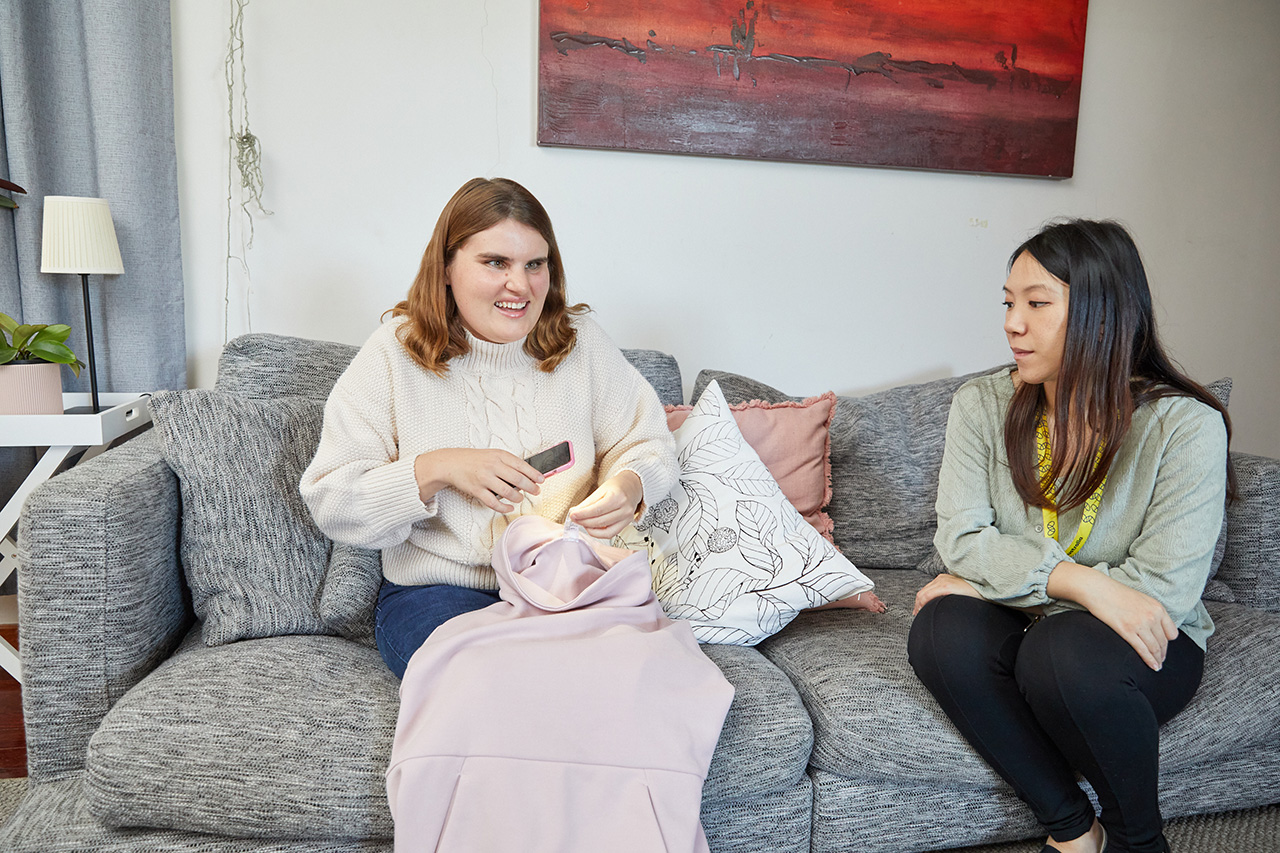 Two women sit on a grey couch