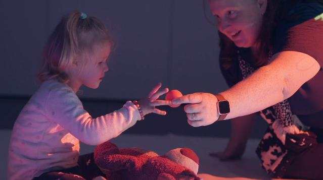 Child reaches for ping pong ball, handed to her by a Vision Australia worker. 